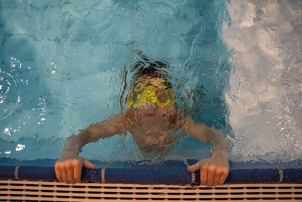 Manos de un nadador agarrando el borde de la piscina, con agua salpicando.
