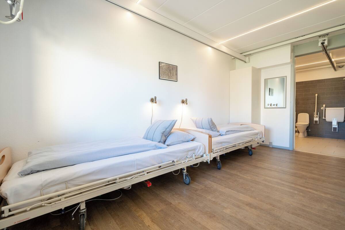 Une chambre d’hôpital avec deux lits, chacun étant équipé d’un oreiller et d’une couverture.
