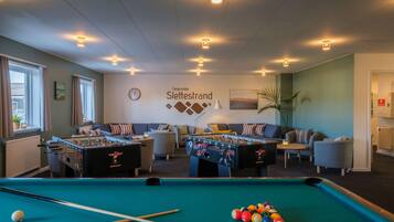 Ett biljardbord, två fotbollsspel, en soffa och en vägg med en klocka och en skylt med texten ”Fiencenter Slettesstrand”.