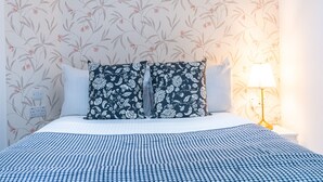 A neatly made bed with a blue and white checkered bedspread, two pillows with a floral pattern, and a bedside lamp on a nightstand. - Fulham 6BR 6BA Tube Family London (London)