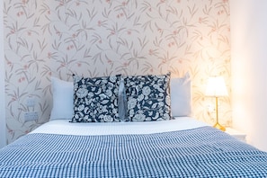 A neatly made bed with a blue and white checkered bedspread, two pillows with a floral pattern, and a bedside lamp on a nightstand. - Fulham 6BR 6BA Tube Family London (London)