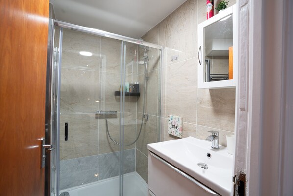 A modern bathroom with a glass-enclosed shower, a white sink, and a mirror above it. - Fulham 6BR 6BA Tube Family London (London)