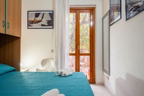 Quarto com cama, guarda-roupa de madeira, quadro emoldurado e porta de vidro deslizante para área externa.