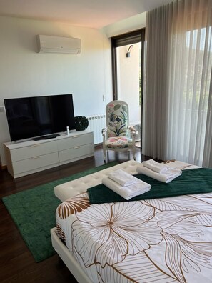 A modern bedroom with a large bed, a flat-screen TV, a white dresser, and a chair with floral upholstery.