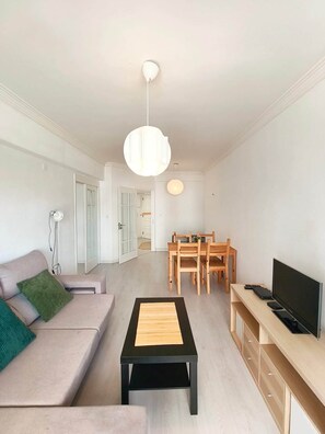 Una sala de estar moderna con un sofá, una mesa de centro, un televisor y un comedor con mesa y sillas.