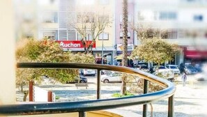 Un balcon avec une balustrade incurvée, une chaise, deux verres à vin et une plante en pot.