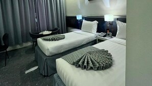 Habitación de hotel con dos camas, un escritorio y una silla. Hay lámparas de noche y un teléfono en las mesitas.