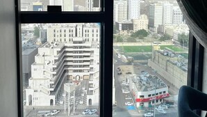 Vista desde una ventana que da a un paisaje urbano con edificios, un estacionamiento y un edificio rojo y blanco con un letrero.