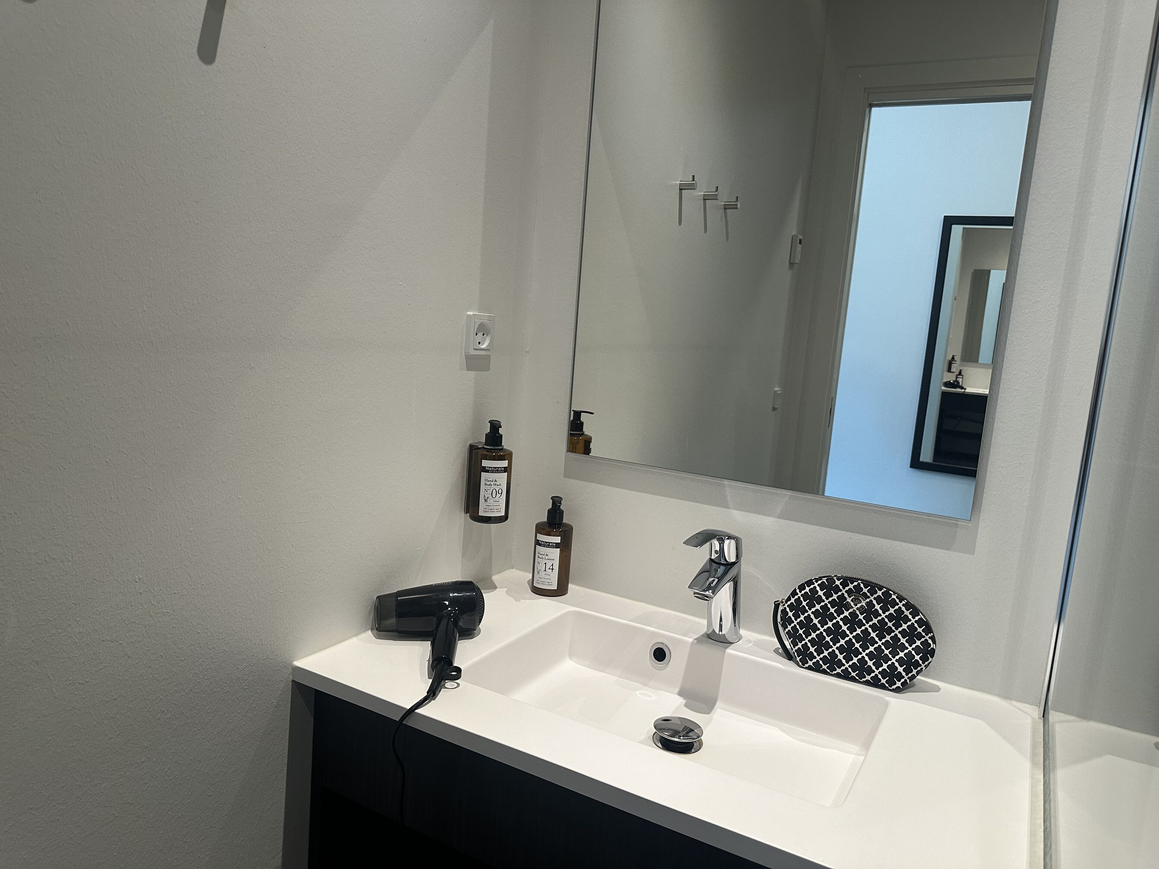 Une salle de bain avec un lavabo blanc, un miroir, un sèche-cheveux et un porte-savon noir et blanc à motifs.
