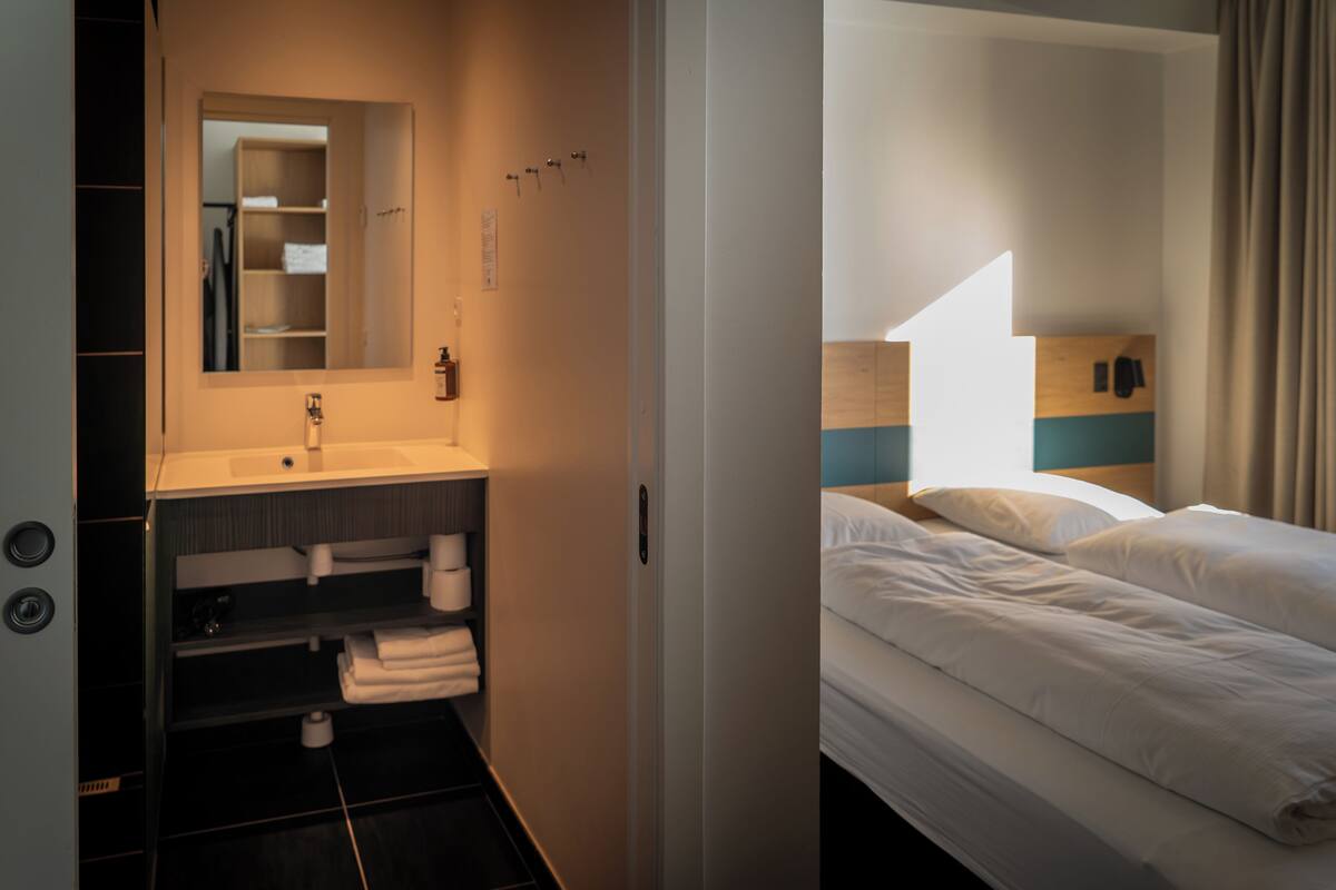Una habitación de hotel con baño, una cama y una mesita de noche.