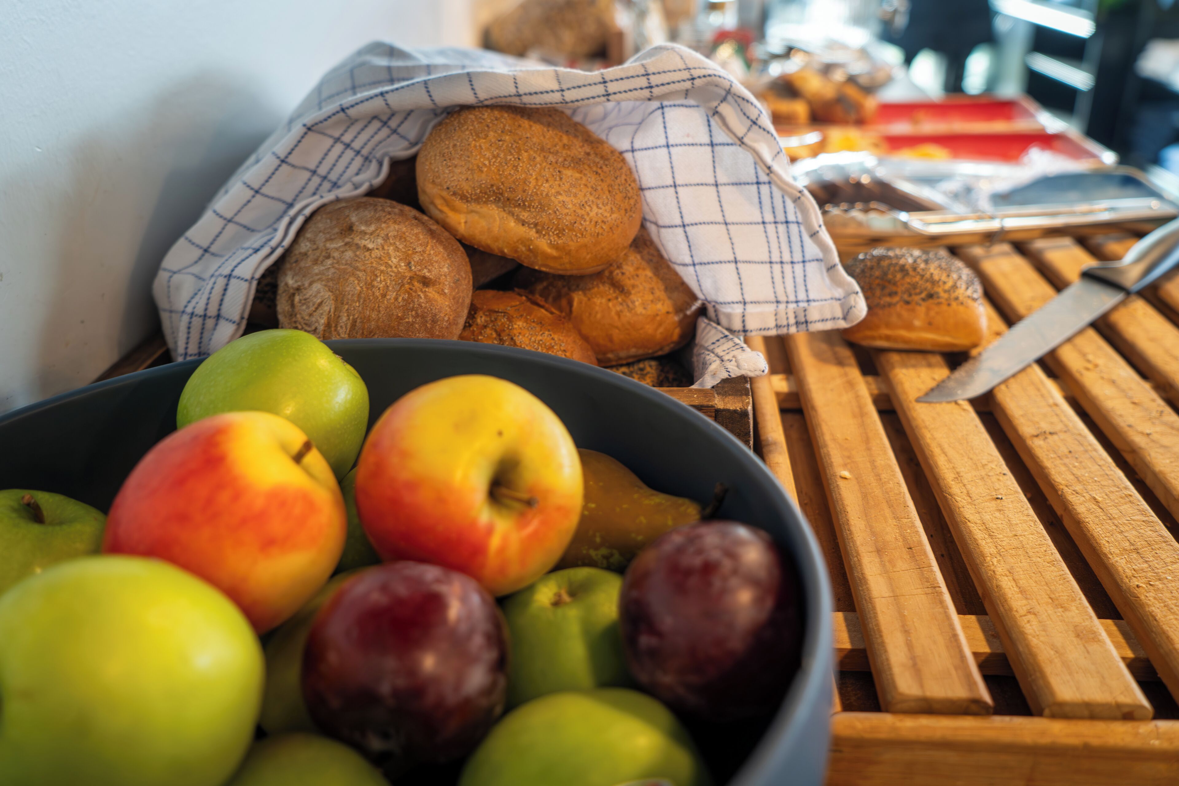 Un bol de manzanas y peras, una bolsa de tela con pan, y un cuchillo sobre una mesa de madera.