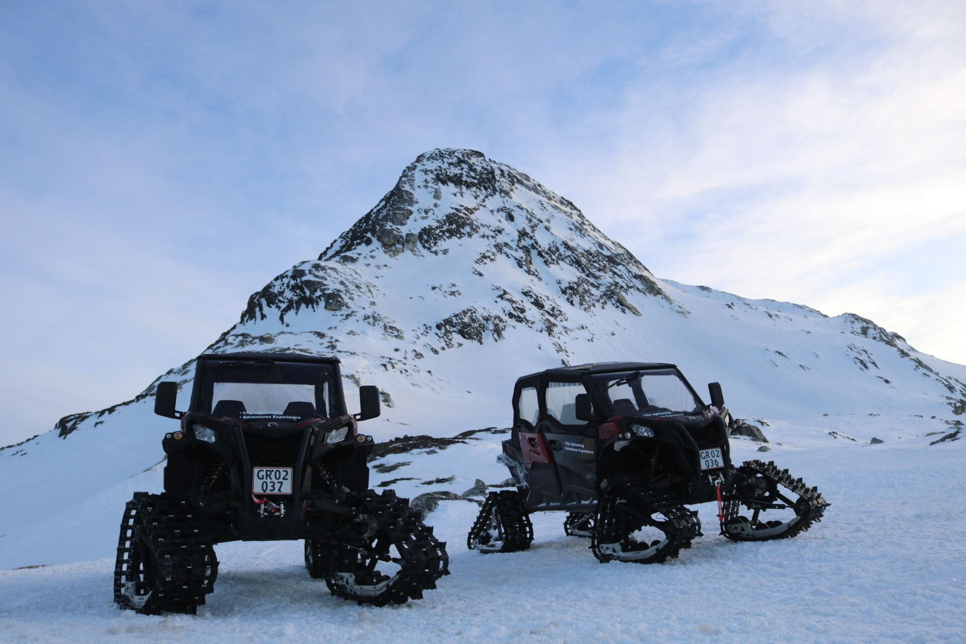 Two snowmobiles parked on a snowy mountain with a large peak in the background.