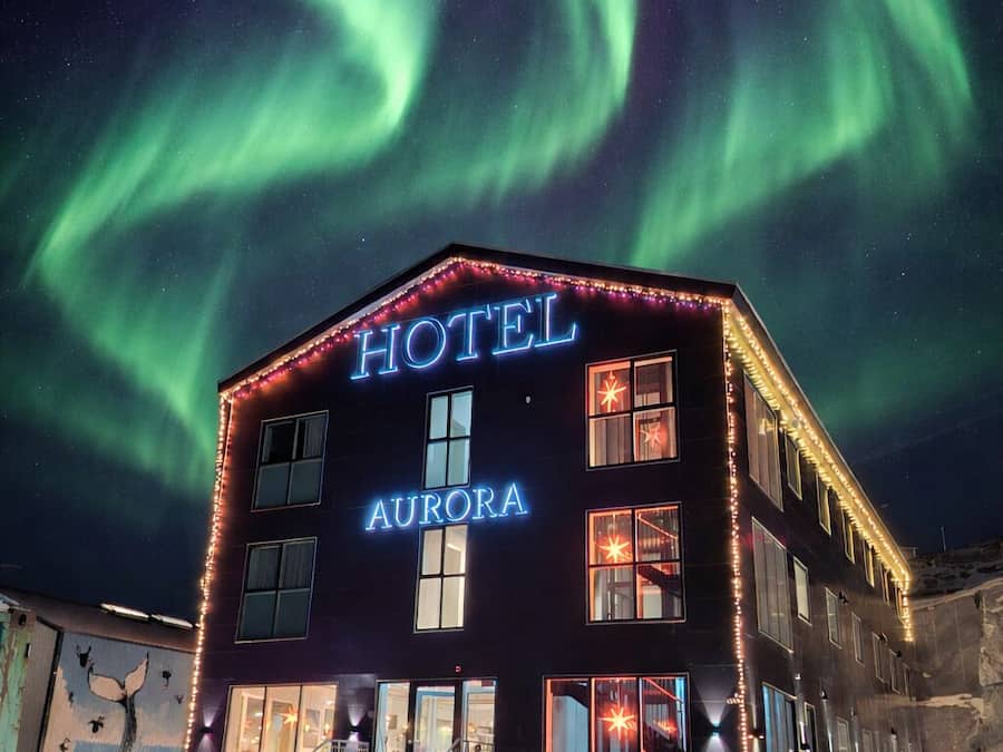 Een hotel met een bord waarop 'HOTEL AURORA' staat, onder een nachthemel met het noorderlicht.