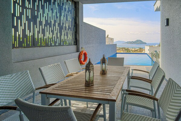 A wooden table with wicker chairs, two lanterns, and a lifebuoy on a balcony with a view of a pool and distant islands. - 4 Bedroom Villa with a private pool and incredible views (Peksimet)