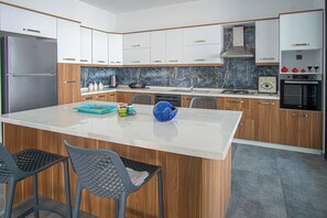 A modern kitchen with a central island, wooden cabinets, a stainless steel refrigerator, and a built-in oven.