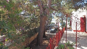 A narrow street with a red metal fence, trees, and a building with red shutters. - Villa Leda in Marina di Mancaversa (Taviano)