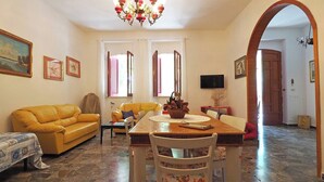A living room with a yellow sofa, a dining table with chairs, a television, and a chandelier. - Villa Leda in Marina di Mancaversa (Taviano)