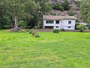 Una casa de dos pisos con techo de tejas, rodeada de un césped cuidado y árboles.