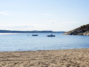 Una playa con dos barcos en aguas tranquilas, costa rocosa y colinas al fondo.