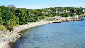 Une zone côtière caractérisée par une plage de sable fin, une côte rocheuse et un paysage urbain en arrière-plan.