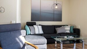 Un salon moderne avec un canapé gris, une table basse en verre et un fauteuil en bois.