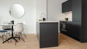 A modern kitchen with a central island, a round mirror, and a dining area with white chairs. - Coopers Cross Two by Dublin At Home (Dublin)