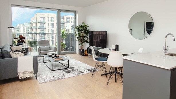 A modern apartment with a living room, dining area, and kitchen. It features a large sliding glass door to the balcony, a flat-screen TV, and a round mirror on the wall. - Coopers Cross Two by Dublin At Home (Dublin)