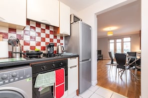 A modern kitchen with a stainless steel refrigerator, a gas stove, and a microwave. There is a dining area with a table and chairs. - Holywell Rise Swords (Swords)