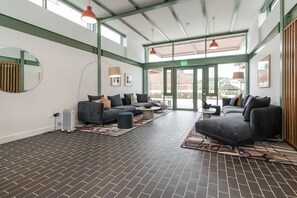 Un hall d’entrée spacieux avec un sol en briques, des canapés gris et un grand miroir.