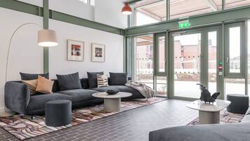 A modern lobby with a grey sofa, round coffee table, and a large window with an exit sign.