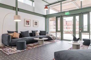 Un hall d’entrée moderne avec un canapé gris, une table basse ronde et une grande fenêtre sur laquelle est apposée un panneau indiquant la sortie.