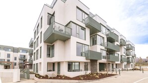 Un moderno edificio residencial de varios pisos, con balcones, ventanas grandes y una entrada porticada.