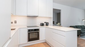 Una cocina moderna con armarios blancos, horno empotrado, cafetera y una pequeña isla con pileta.