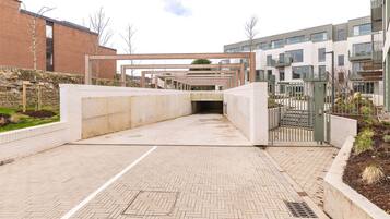 A modern building entrance with a brick facade, a covered walkway, and a gated area with a metal fence.