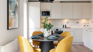 A modern kitchen with white cabinets, a built-in oven, and a dining area with a round table and yellow chairs. - The Oslo by Dublin At Home (Dublin)