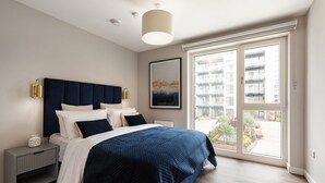 A modern bedroom with a large bed, a bedside table, a nightstand, a window with a view of buildings, and a ceiling light. - The Oslo by Dublin At Home (Dublin)