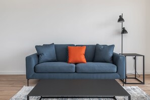 A modern living room with a dark blue sofa, an orange pillow, a black coffee table, and a floor lamp. - The Cornerstone Two by Dublin At Home (Dublin)