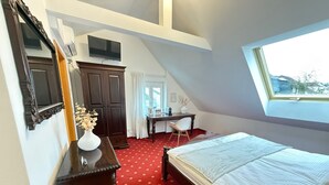 Ein Schlafzimmer mit Bett, Schreibtisch, Stuhl, Kommode, Fernseher und Fenster.