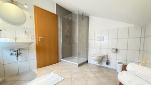 Ein modernes Badezimmer mit Waschbecken, Spiegel, Toilette, Dusche und einer Holzbank.