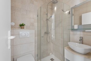 Ein modernes Badezimmer mit einer gläsernen Duschkabine, einem weißen Waschbecken und einem kleinen Topfpflanzen an der Wand.