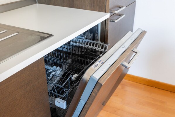 An open dishwasher in a kitchen with a white countertop and wooden cabinets.