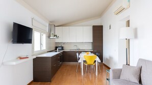A modern kitchen with white cabinets, a dining table with yellow chairs, and a grey sofa in a bright living area. - Attico Eleonora – Terrazza & Parcheggio in Centro (Oristano)