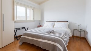 A bedroom with a bed, a window, a nightstand, and a wall-mounted shelf. - Attico Eleonora – Terrazza & Parcheggio in Centro (Oristano)