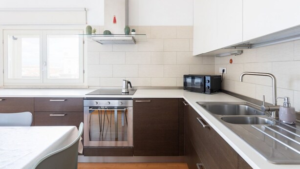 A modern kitchen with a stove, microwave, and double sink. - Attico Eleonora – Terrazza & Parcheggio in Centro (Oristano)