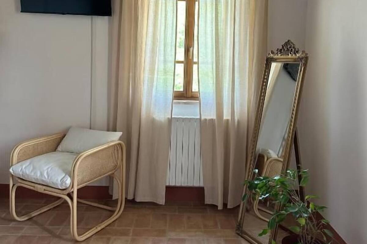 A room with a wicker chair, a potted plant, a mirror, and a window with curtains.