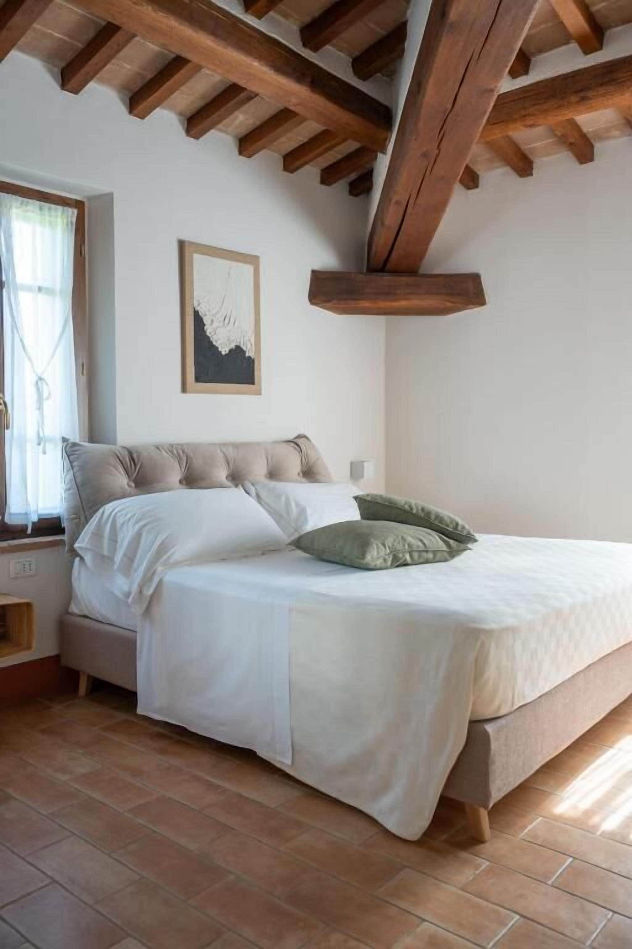 Une chambre à coucher avec un lit, des poutres en bois, une fenêtre avec des rideaux et un tableau encadré au mur.