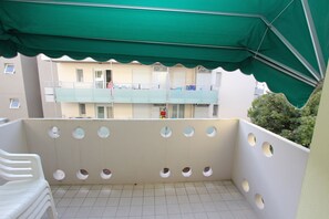 A balcony with a green awning, tiled floor, and multiple circular cutouts in the wall. - Comfy Flat by the Beach (San Michele al Tagliamento)