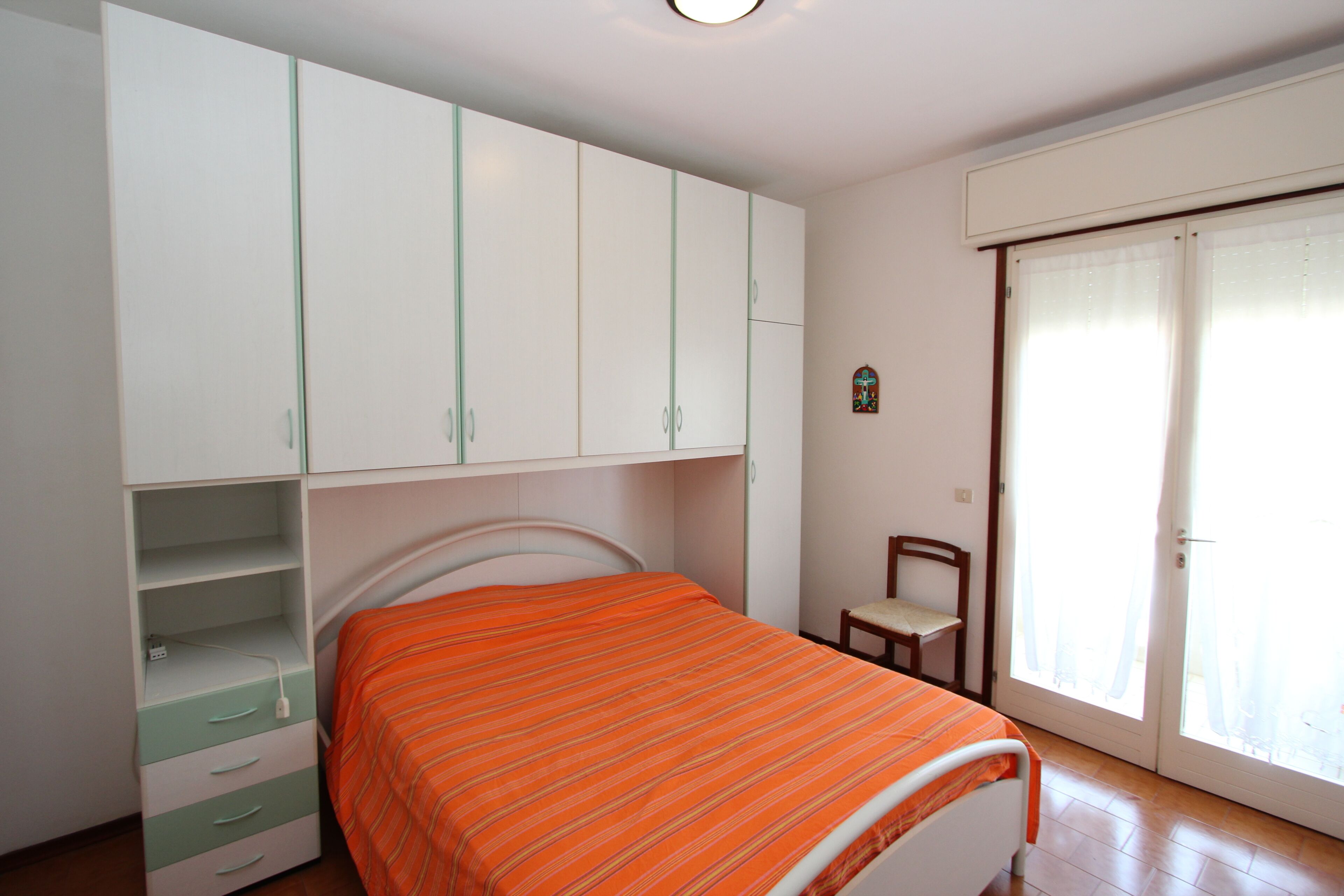 Ein Schlafzimmer mit Bett, Kleiderschrank, Stuhl und Fenster.