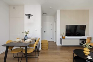 Ein modernes Wohnzimmer mit Essbereich, mit einem schwarzen Esstisch, gelben Stühlen, einem schwarzen Couchtisch und einem Fernseher, der an einem weißen Schrank befestigt ist.