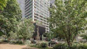 Un immeuble moderne à plusieurs étages, entouré d’une végétation luxuriante et de voitures garées.